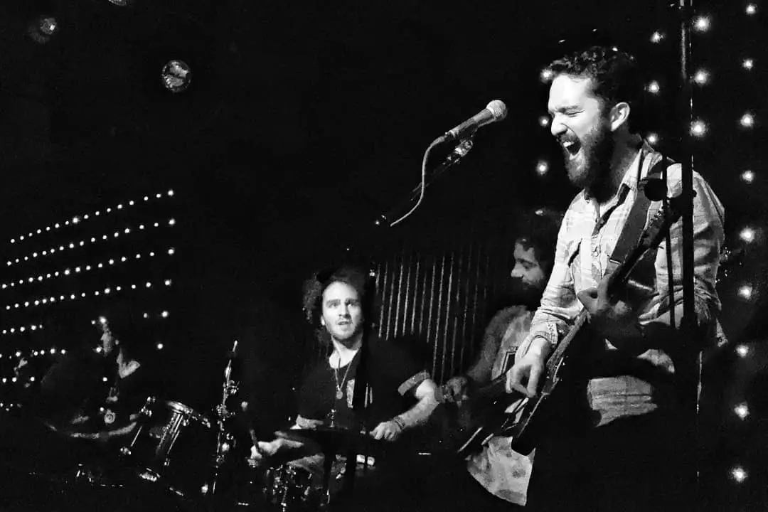 Stephen singing and playing guitar on stage with his band, in black and white.